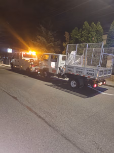 Intervenție de seară pe stradă: tractarea unui camion mic de marfă, cu ladă deschisă și grilaj metalic pentru transport, inscripționat "Transport orice tip de marfă".